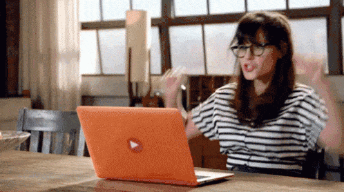 Mulher mexendo em um laptop laranja.