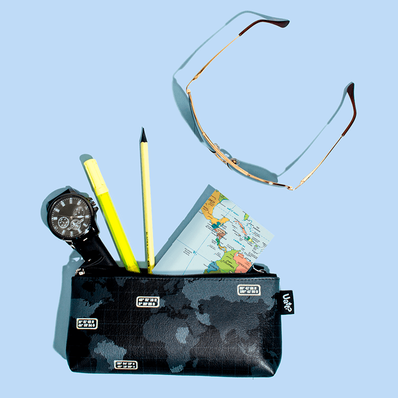 Fundo azul com um óculos e uma necessaire entreaberta, com um bloco de notas, um relógio e canetas.