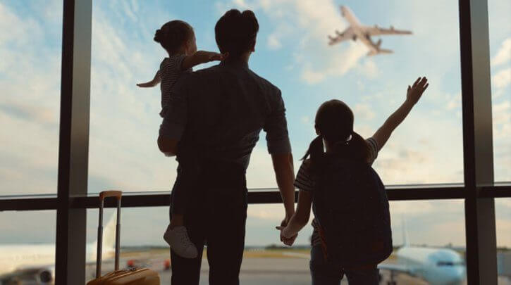 pai e seus dois filhos observando viagens de avião através de uma vidraça de aeroporto