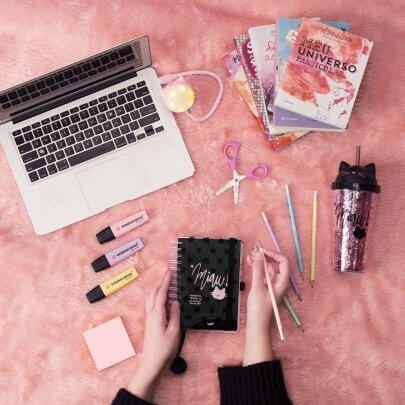 fundo rosa com notebook, livros, lápis de grafite, agenda, copo com canudo e marca-textos.