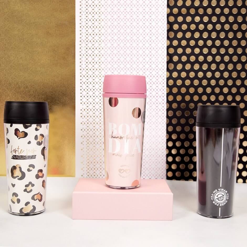 mesa com três copos térmicos, um com estampa de onça, outro rosa e outro preto.