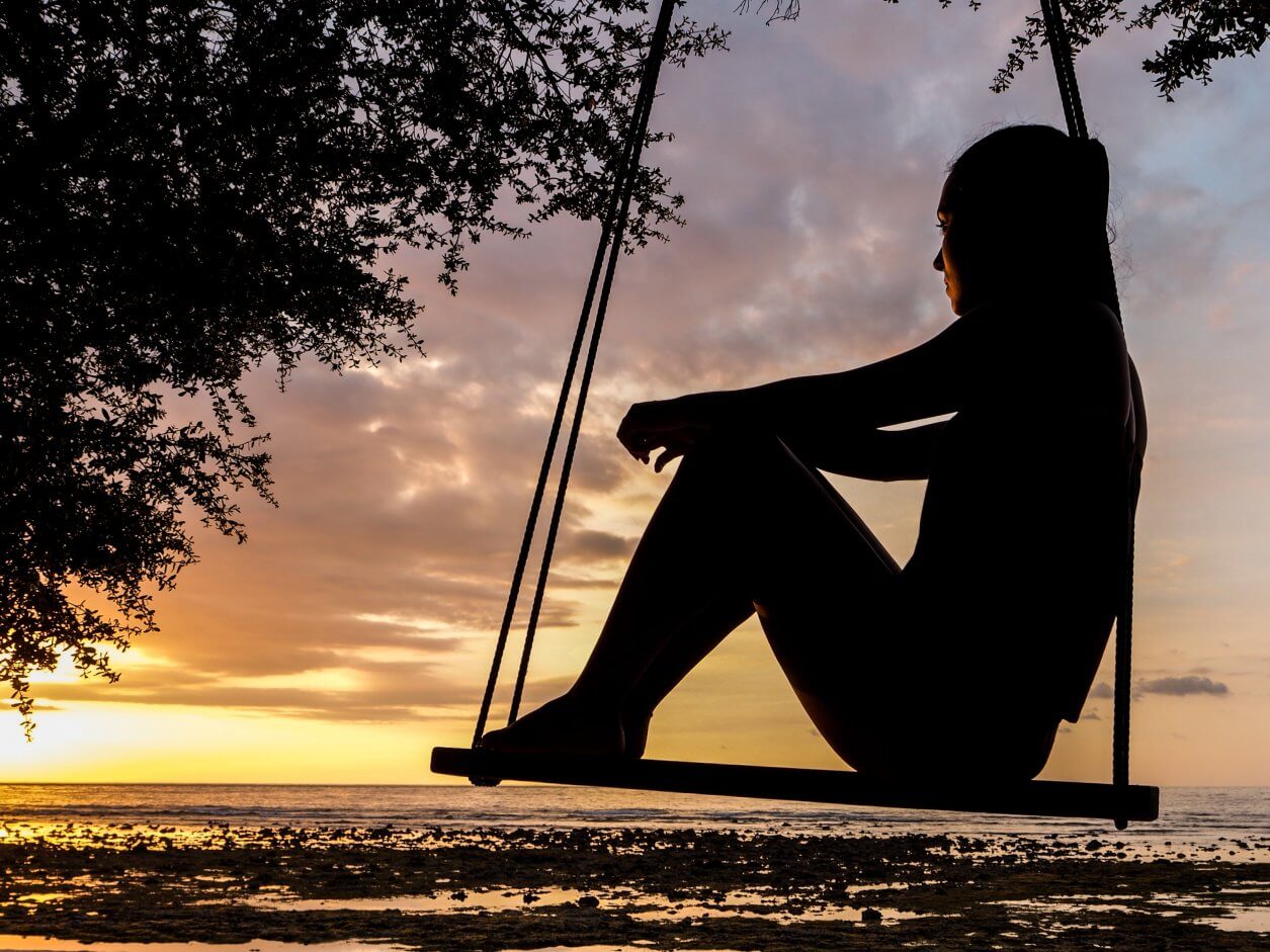 silhueta de uma mulher sentada em um balanço admirando o nascer do sol.