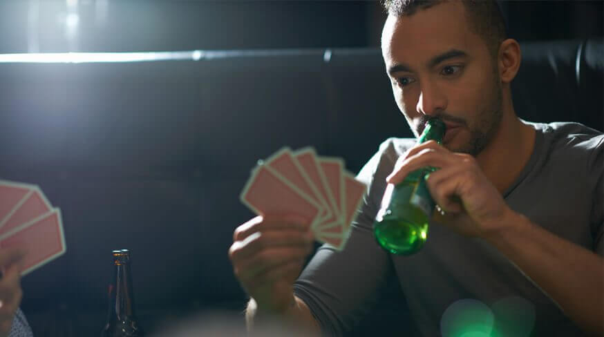 homem bebendo cerveja enquanto segura um baralho de jogos de bebida