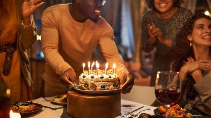 homem segurando um bolo de aniversário com pessoas batendo palmas ao redor
