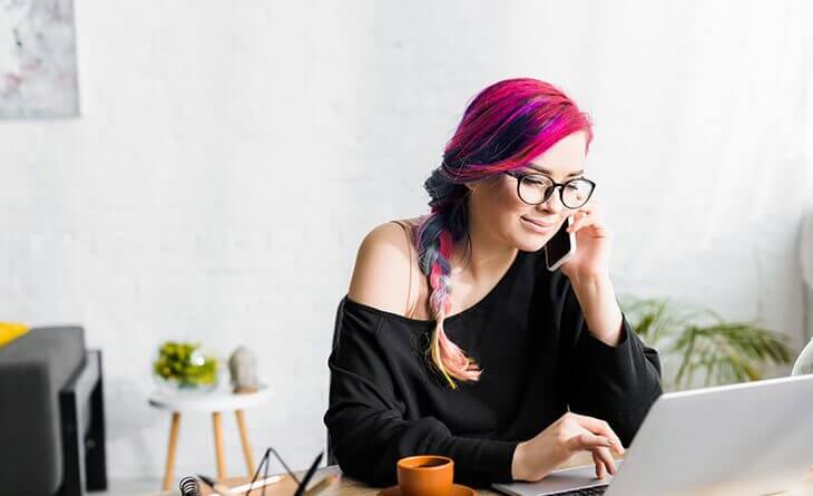 mulher com cabelo rosa e azul e óculos falando no celular